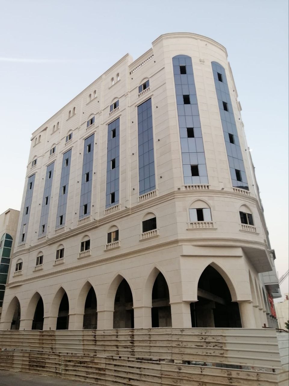 مبنى بيج متعدد الطوابق بأقواس في الطابق الأرضي ولوحات زجاجية زرقاء