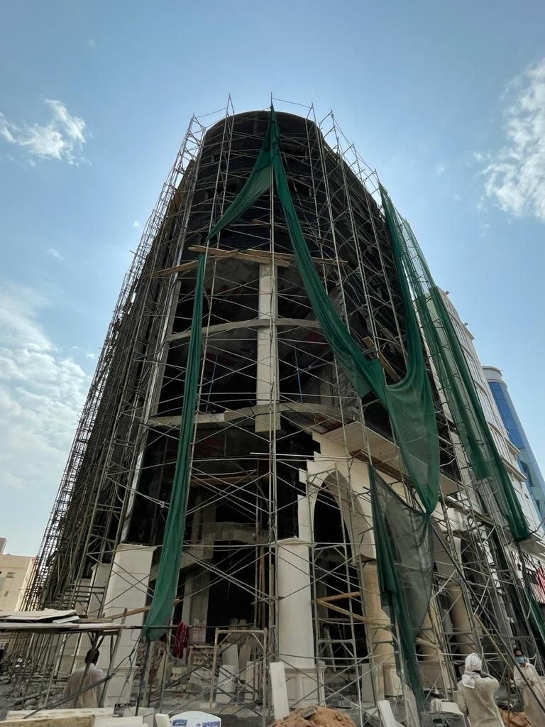 المبنى خرسانة مكشوفة محاطة بسقالات وشبكة أمان خضراء