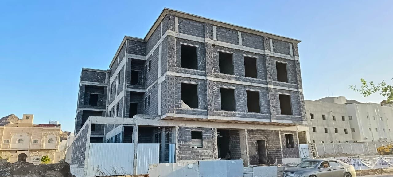 العمارة قبل التشطيب: بلوك رمادي بفتحات نوافذ مفتوحة وعوارض خرسانية ظاهرة